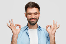 Hey, I Got Ot! Pleased Satisfied Caucasian Male With Thick Beard, Says That Everything Is Okay And Under Control With Gesture, Keeps Eyes Closed, Has Joyful Expression, Isolated Over White Background.