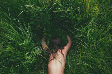 Wall Mural - young brunette woman enjoying the lying on green fresh grass facedown. top view.