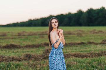 Beautiful young girl in a long sundress at sunset in the fields posing.