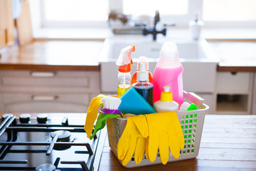 Basket with cleaning items on blurry background white citchen. Cleaning concept.