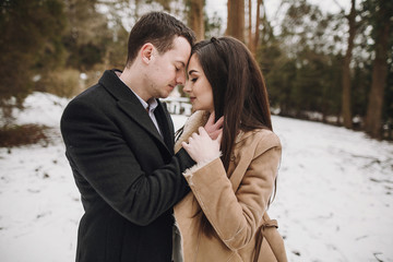 Wall Mural - gorgeous wedding couple hugging in winter snowy park. stylish bride in coat and  groom embracing under  trees in winter forest. romantic sensual moment of newlyweds