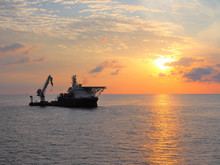Construction Support Vessel Positions Next To Static Platform With Sun Rise Background.