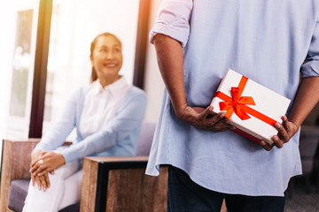 Middle aged husband hiding a surprise gift and roses for surprising his wife on special day such as birthday or wedding anniversary. Celebration and holiday concept