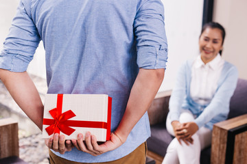 Wall Mural - Teenage son hiding a surprise gift and giving to senior mother on her special day such as mother's day or birthday. Celebration and holiday concept