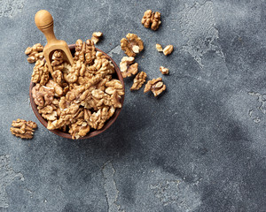 Walnut kernels with wooden scoop on gray background with copy space. Nuts in clay bowl. Top view.