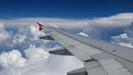 Wall Mural - 4K footage airplane flight. wing of an airplane flying above the white clouds and blue sky. beautiful aerial view from the window of the plane on travelling time by aircraft. holiday , vacation time