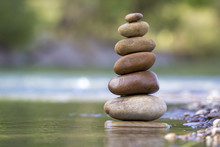 Close-up Abstract Image Of Wet Rough Natural Brown Uneven Different Sizes And Forms Stones Balanced Like Pyramid Pile Landmark In Shallow Water On Blurred Blue-green Misty Copy Space Background.