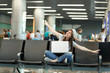 © ViDi Studio - Young funny traveler tourist woman with laptop sit with crossed legs spreading hands as in flight, waiting in lobby hall at airport. Passenger traveling abroad on weekend getaway. Air flight concept.