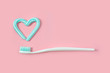 Toothbrushes and turquoise color toothpaste in shape of heart on pink background. Dental and healthcare concept.