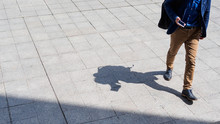 Business Man Walking And Texting On His Mobile Phone On Pedestrian With Black Silhouette Shadow On Ground. 