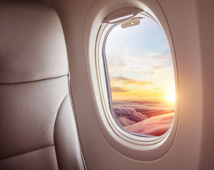 Wall Mural - airplane interior with window view of sunset above clouds.