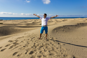 Fascinated young man in Maspalomas sand dunes, Canary Islands. Tourist with open arms enjoying views of popular desert landmark in Gran Canaria, Spain. Summer vacation, travel destination concepts