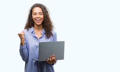 Young hispanic woman holding computer laptop screaming proud and celebrating victory and success very excited, cheering emotion