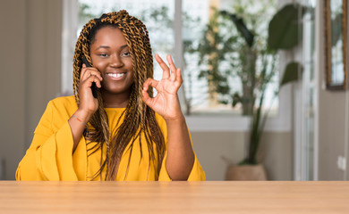 Wall Mural - African american woman using smartphone doing ok sign with fingers, excellent symbol