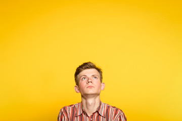 Wall Mural - serious concentrated handsome man looking up. portrait of a young guy on yellow background popping up or peeking out from the bottom. copyspace for advertisement.