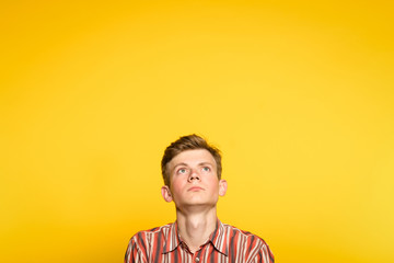 serious concentrated handsome man looking up. portrait of a young guy on yellow background popping up or peeking out from the bottom. copyspace for advertisement.