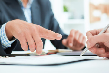 Male boss recommends that his employee sign a contract in the office. Business man points to the place where it is necessary to put the signature.