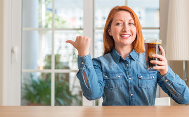 Sticker - Redhead woman holding soda refreshment pointing with hand and finger up with happy face smiling