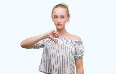 Sticker - Blonde teenager woman wearing a bun with angry face, negative sign showing dislike with thumbs down, rejection concept