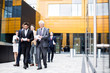 © pressmaster - Team of elegant colleagues in suits discussing papers and working moments while walking along modern building