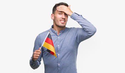 Sticker - Handsome young man holding a flag of Germany stressed with hand on head, shocked with shame and surprise face, angry and frustrated. Fear and upset for mistake.