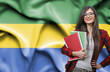 Happy female student holdimg books against national flag of Gabon