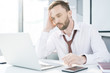 © Seventyfour - Portrait of tired handsome businessman wearing shirt and tie using laptop while working at desk in office