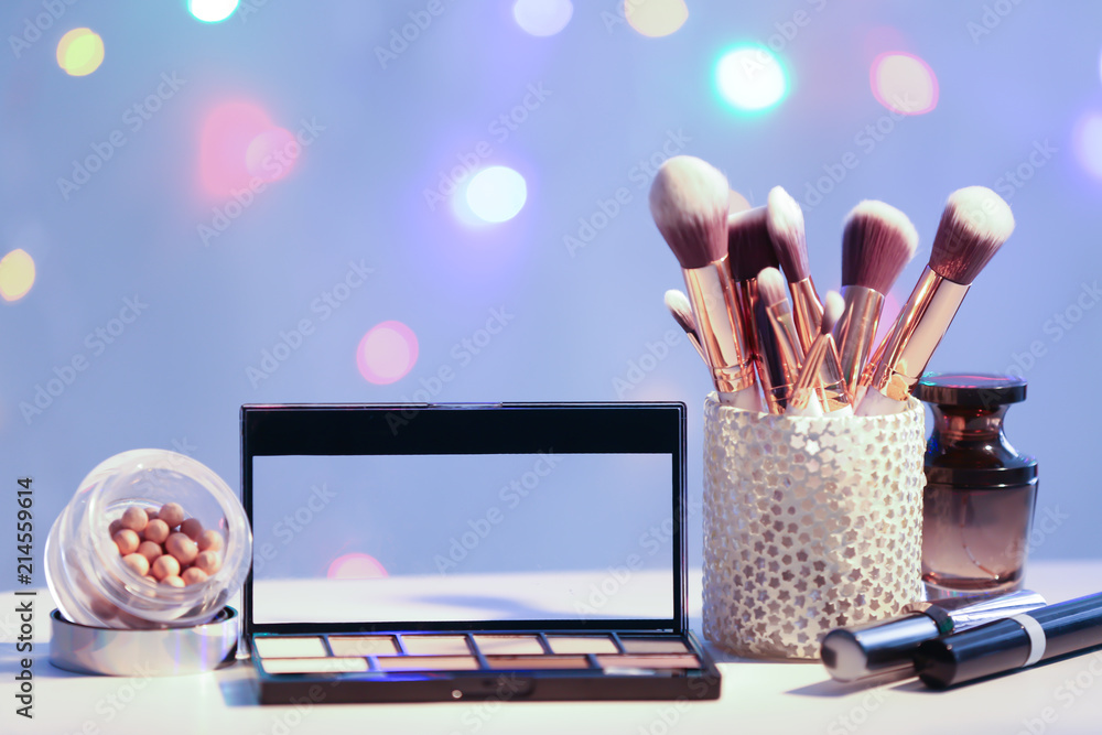 Set of decorative cosmetics with brushes on table against blurred lights