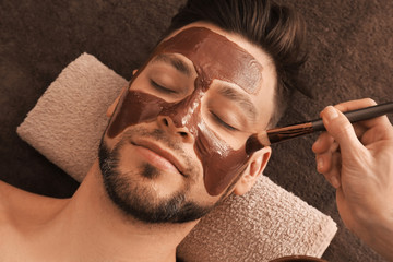 Wall Mural - Beautician applying cosmetic mask on man's face in spa salon