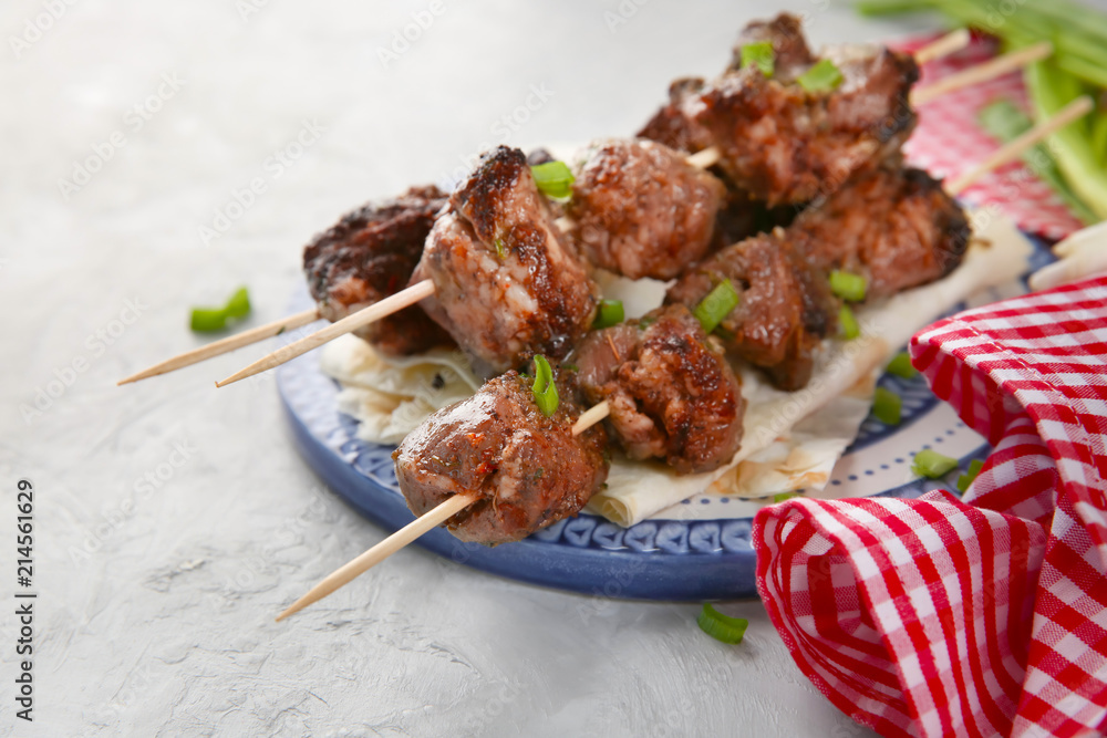 Plate with juicy meat on barbecue skewers on table