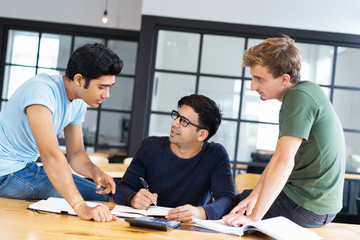 Three multiethnic fellow students doing homework together. Young men sitting on desk and discussing task. Education and students concept.