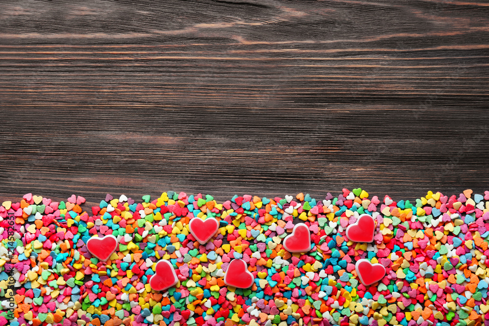 Many heart-shaped candies on wooden background