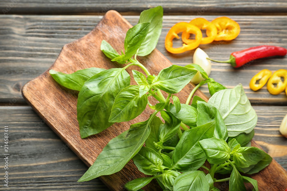 Wooden board with fresh basil on table