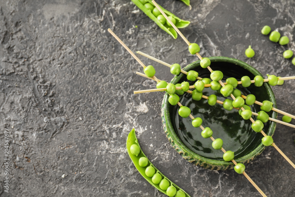Bowl and skewers with fresh green peas on grey textured background