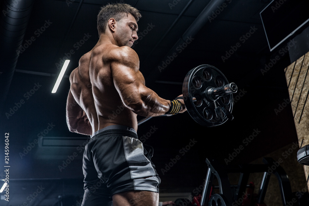 A young brutal male athlete is a bodybuilder with a perfect abs, exercising in the gym. Concept - strength, bodybuilding, styrodes, weightlifting, diet, muscles, sports nutrition, personal trainer - obrazy, fototapety, plakaty 
