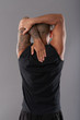 Back view of tattooed fit man holding hands raised and warming up muscles standing on gray background
