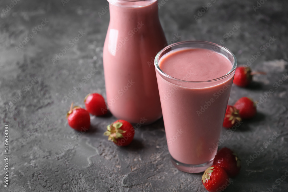 Glass and bottle with strawberry smoothie on grey table