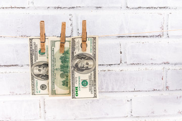 Three 100 USD bills hanging on the string attached with old wooden washing clips on the white shabby bricks background