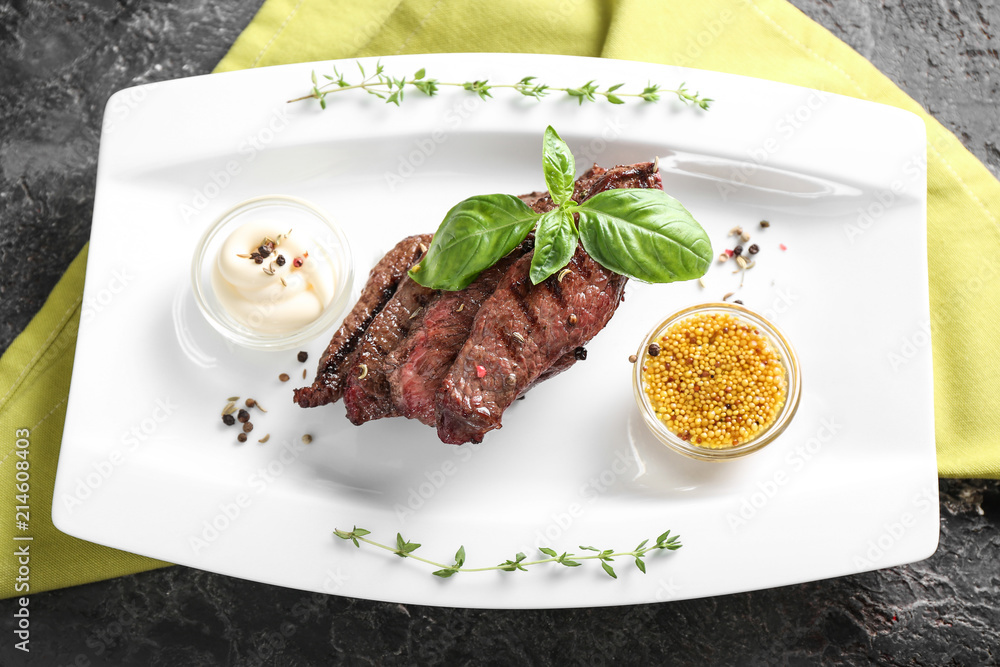 Tasty grilled meat with basil, sauces and spices on plate