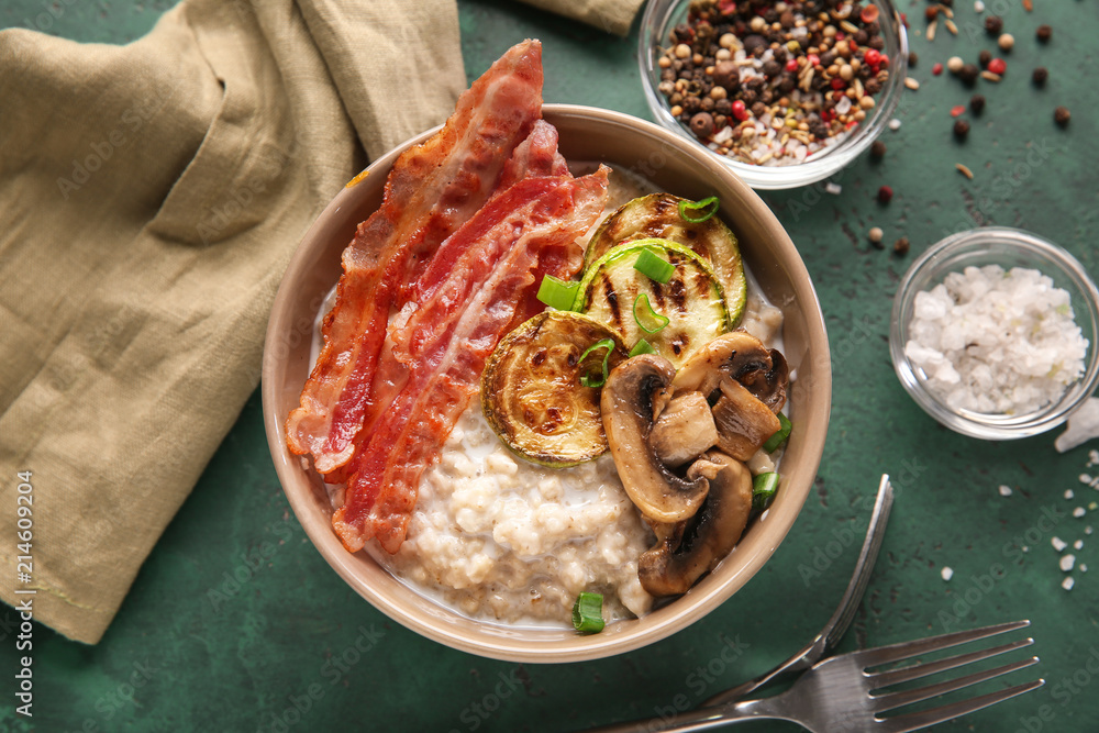 Bowl with tasty oatmeal, fried bacon, mushroom and squash on table