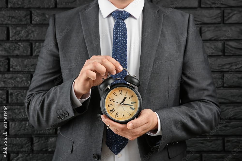 Businessman with alarm clock against brick wall. Time management concept