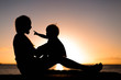© globalmoments - Mother and child playing and watching sunset on the beach in silhouette
