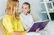 © LIGHTFIELD STUDIOS - smiling mother and daughter sitting on couch and reading book at home