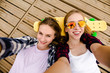 © Leika production - Two young girl in hipster outfit making selfie while lying with on wooden pier