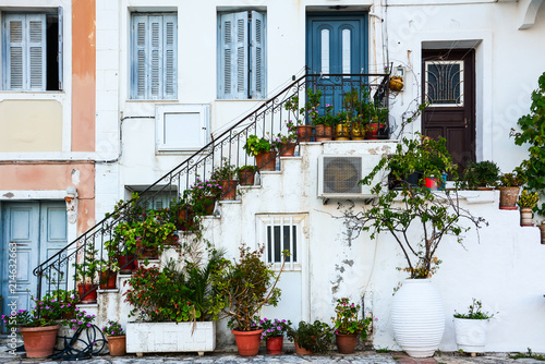blue-door-and-blue-windows-on-a-traditional-greek-white-facade-with-stairs-and-pots-full-of-flowers-in-the-afternoon