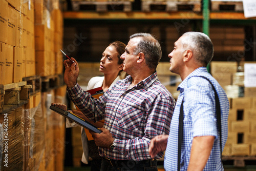 Fotografía Team of customs managers and warehouse worker checking list and inventory on the shelf in storehouse
