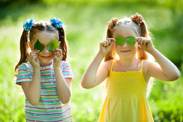 Wall Mural - two beautiful little girls in the summer in a park with leaves in hands