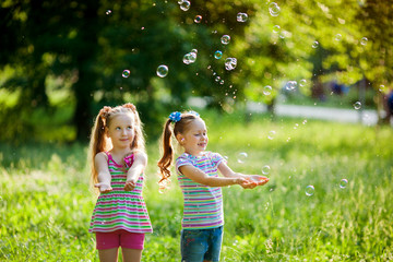 Wall Mural - two beautiful little girls in the summer playing in the park with soap bubbles