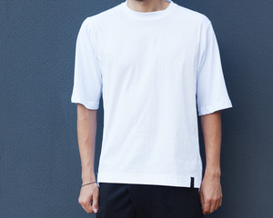 Youth street fashion for men. A man in the afternoon on a summer street in a fashionable outfit against the gray wall. White trendy T-shirt. Part of the body.