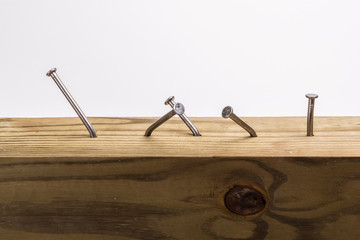 Steel nails, straight and crooked, hammered into a wooden board